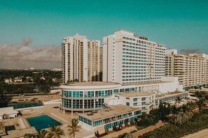 A high-rise hotel with multiple floors, a swimming pool, and a landscaped area with palm trees.