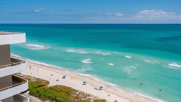 Ein Strandhotel mit Balkon und Blick auf den Ozean, einen Sandstrand und klares, blaues Wasser.