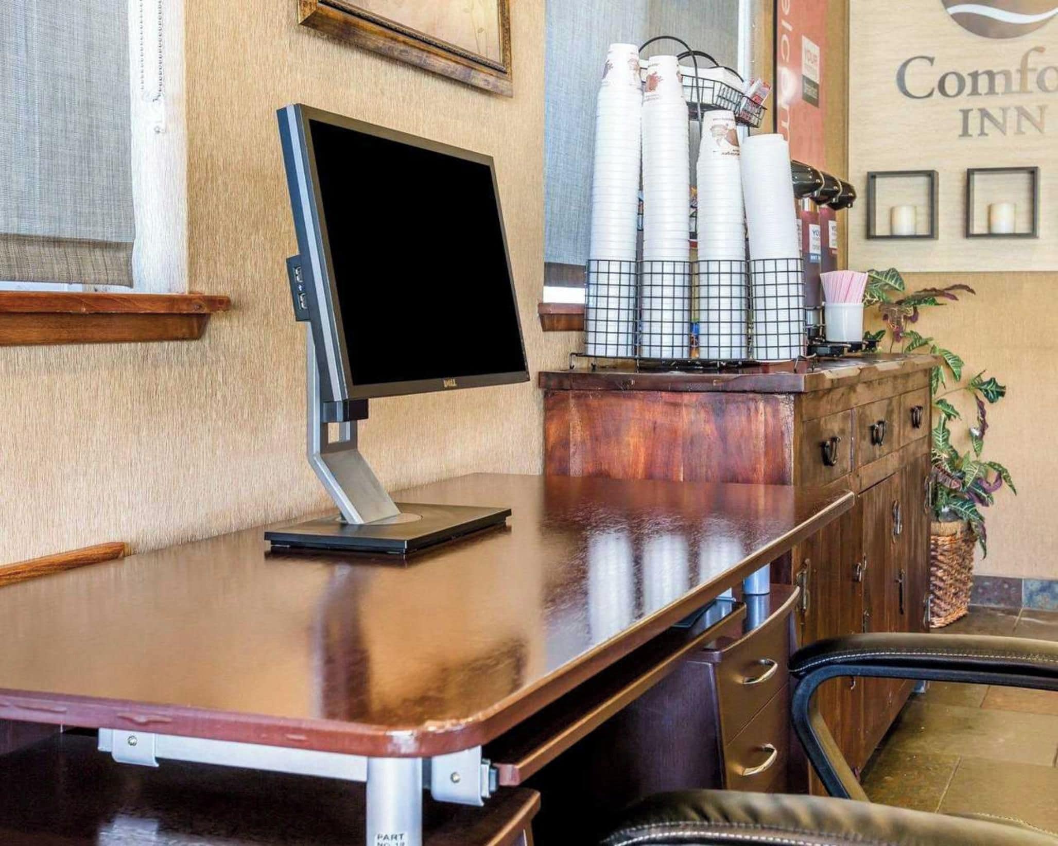 Een receptiebalie met een computerscherm, een plant en een muur met een bord.