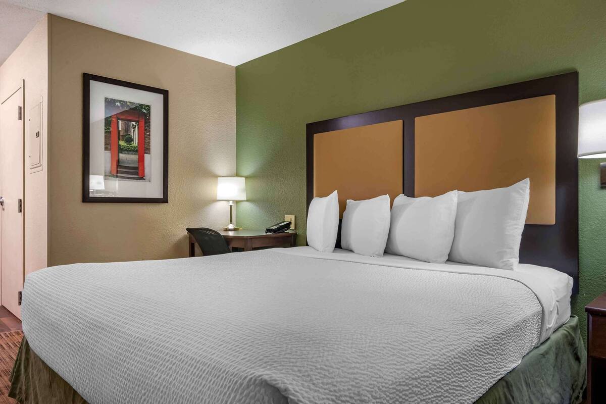 A hotel room with a large bed, a nightstand with a lamp, and a framed picture on the wall.