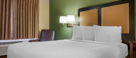 A hotel room with a large bed, a chair, a wall-mounted lamp, and a window with curtains.