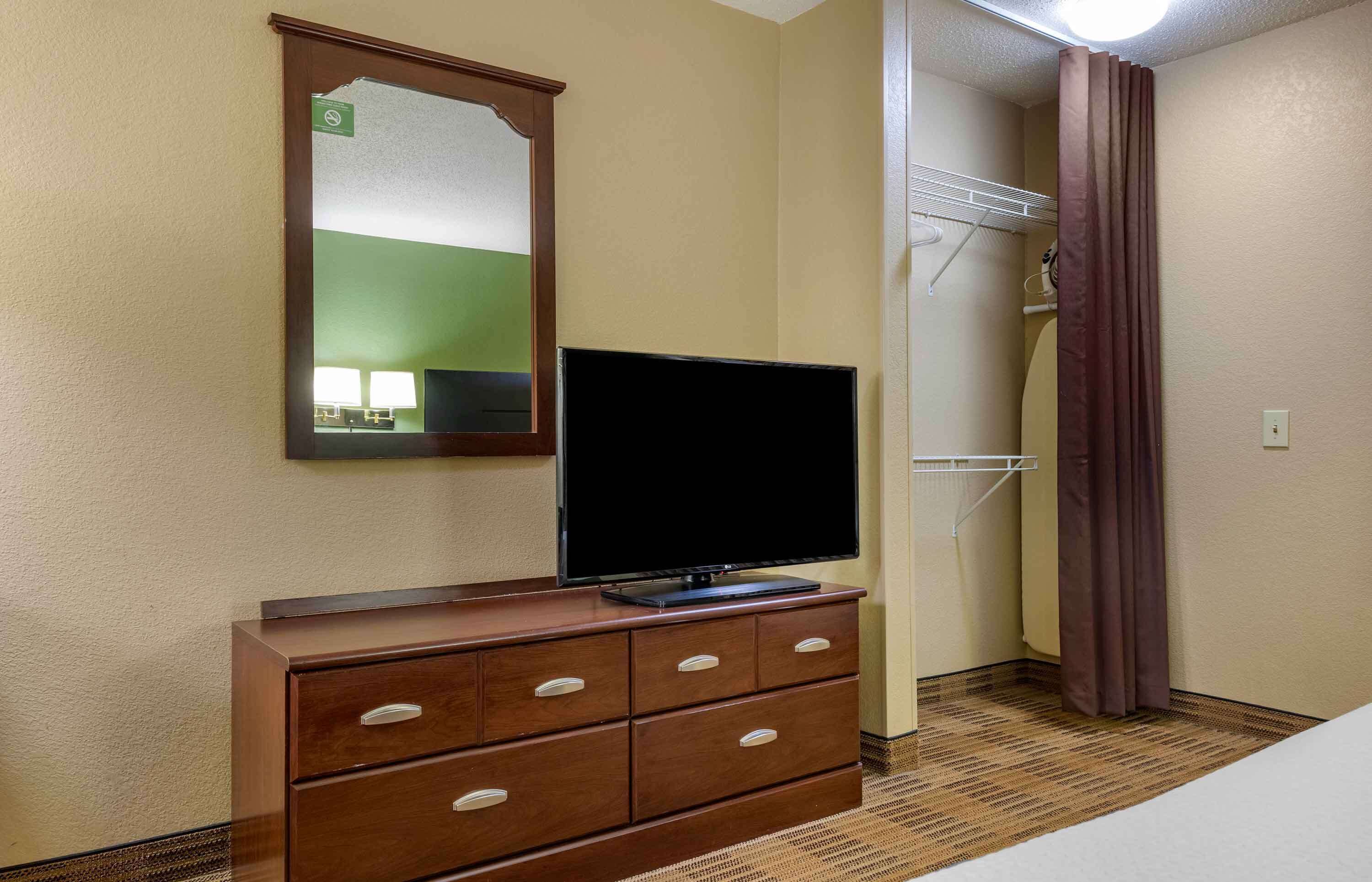 Ett hotellrum med en byrå i trä, en platt-TV, en spegel och en duschhörna med duschdraperi.