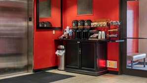 A red-walled room with a coffee station, a trash bin, and an exit door.