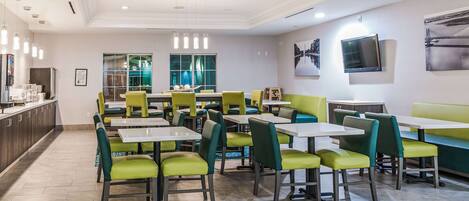 A modern restaurant with green and white seating, a large window, and a flat-screen TV on the wall.