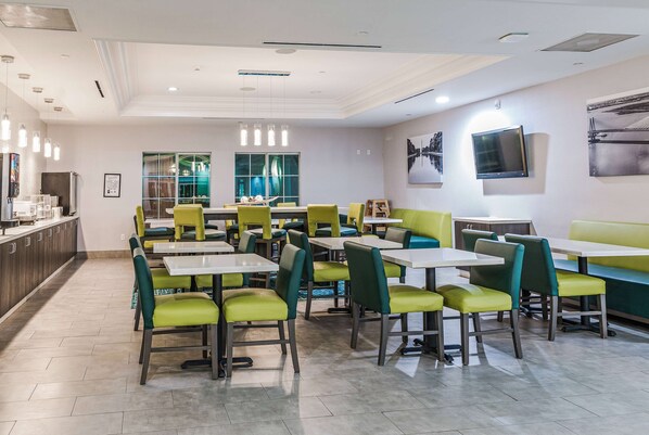 A modern restaurant with green and white seating, a large window, and a flat-screen TV on the wall.