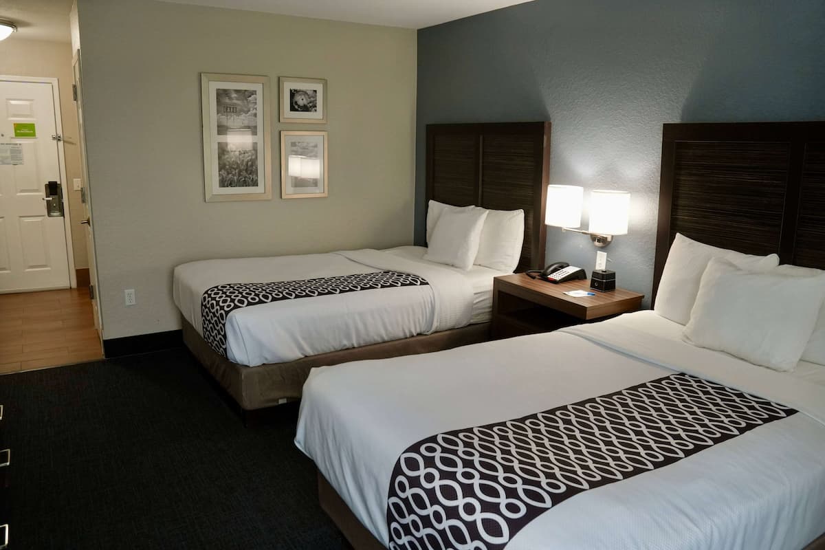 A hotel room with two beds, a nightstand with a lamp, and framed pictures on the wall.