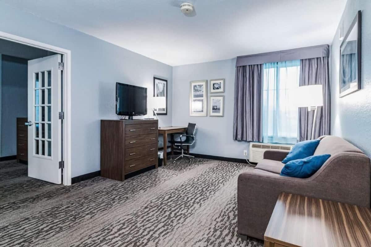 A hotel room with a sofa, a TV, a desk, a chair, a dresser, and a door.
