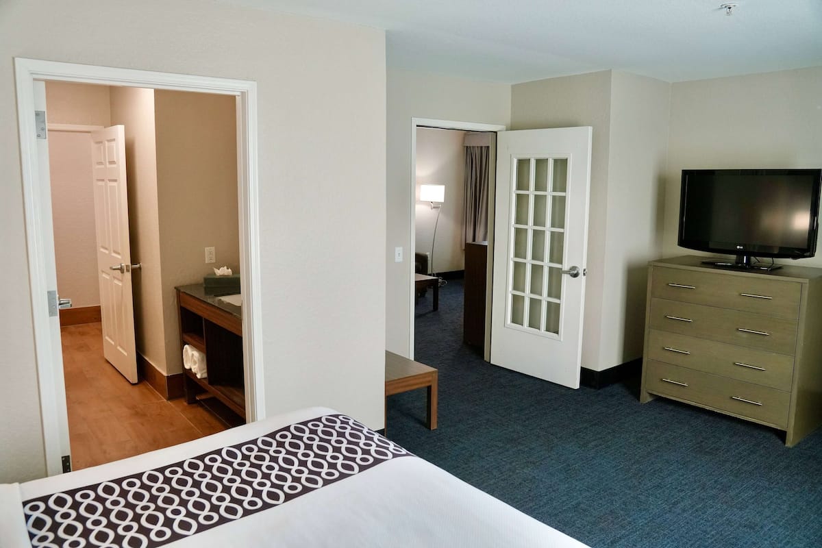 A hotel room with a bed, a dresser, a television, and a bathroom visible through an open door.