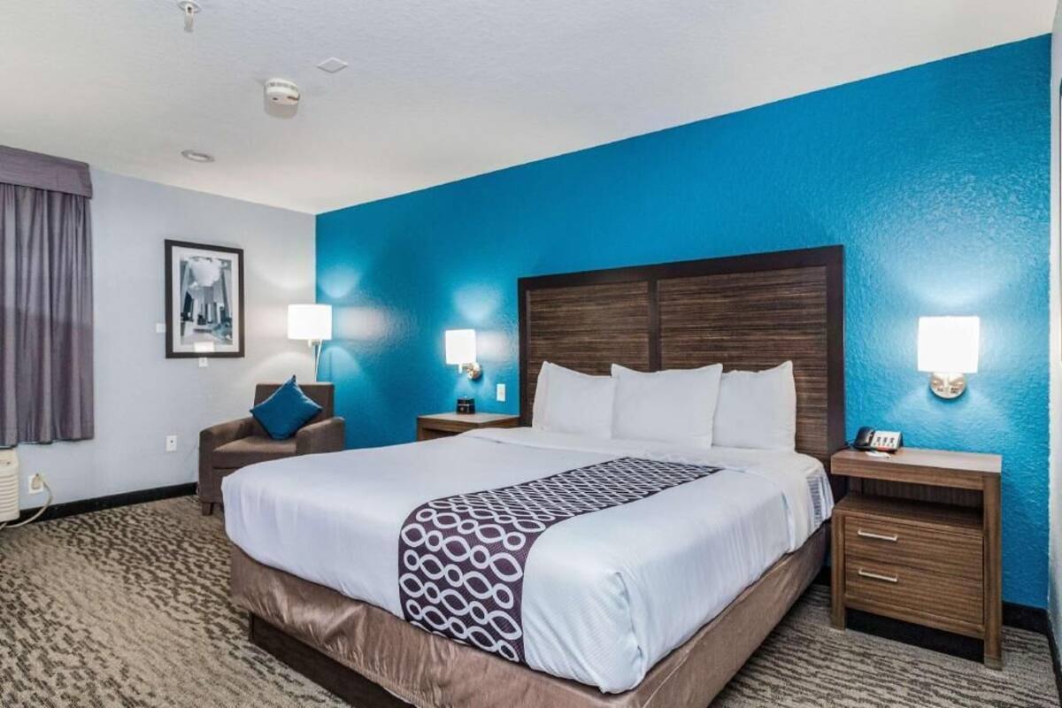 A hotel room with a large bed, two bedside tables, a chair, and a wall-mounted lamp.