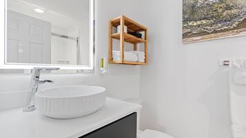 A modern bathroom with a white sink, a wooden shelf, and a painting on the wall.
