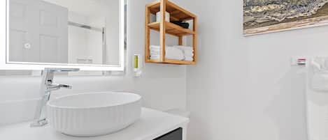 Un baño moderno con un lavabo blanco, un estante de madera y un cuadro en la pared.