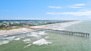A pier extending into the ocean with a beach and residential area in the background. - Ocean Isle Inn (Ocean Isle Beach)