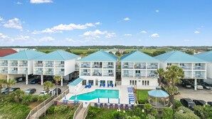 A multi-story hotel with a swimming pool, balconies, and a parking area. - Ocean Isle Inn (Ocean Isle Beach)