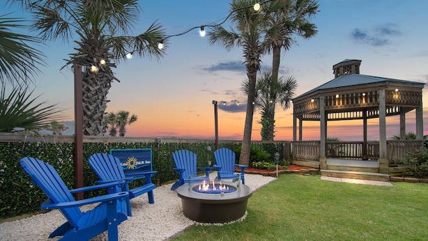 A patio area with Adirondack chairs, a fire pit, and a gazebo. - Ocean Isle Inn (Ocean Isle Beach)
