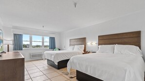 A hotel room with two beds, a desk, a window with curtains, and a view of the outside.