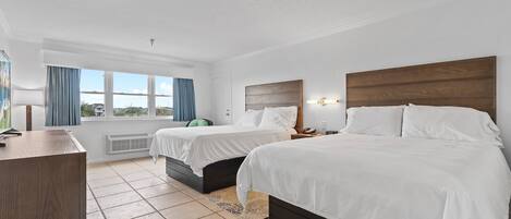 Ett hotellrum med två sängar, ett skrivbord, ett fönster med gardiner och utsikt över omgivningen.