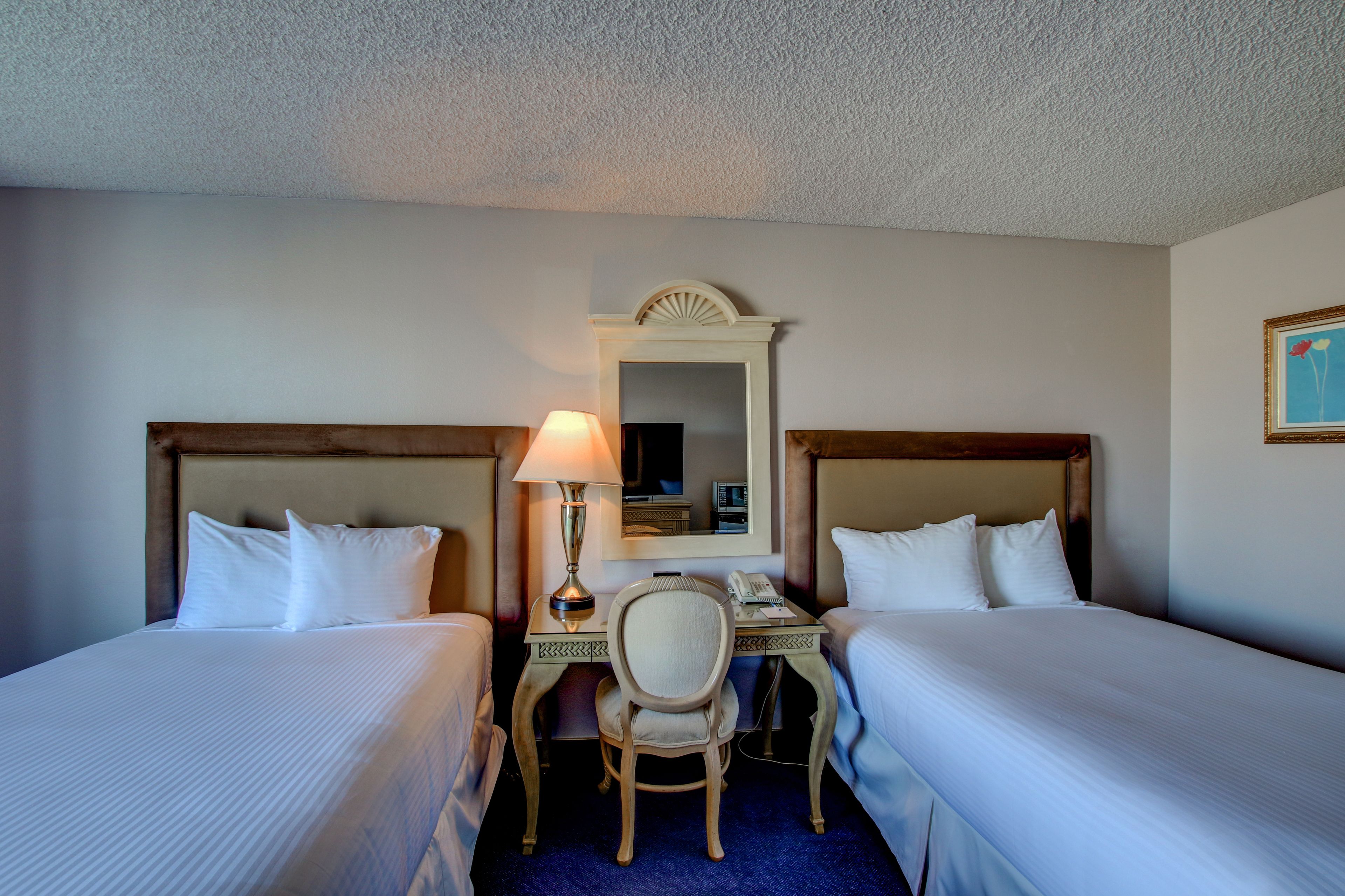 A hotel room with two beds, a desk, a chair, a lamp, and a mirror.