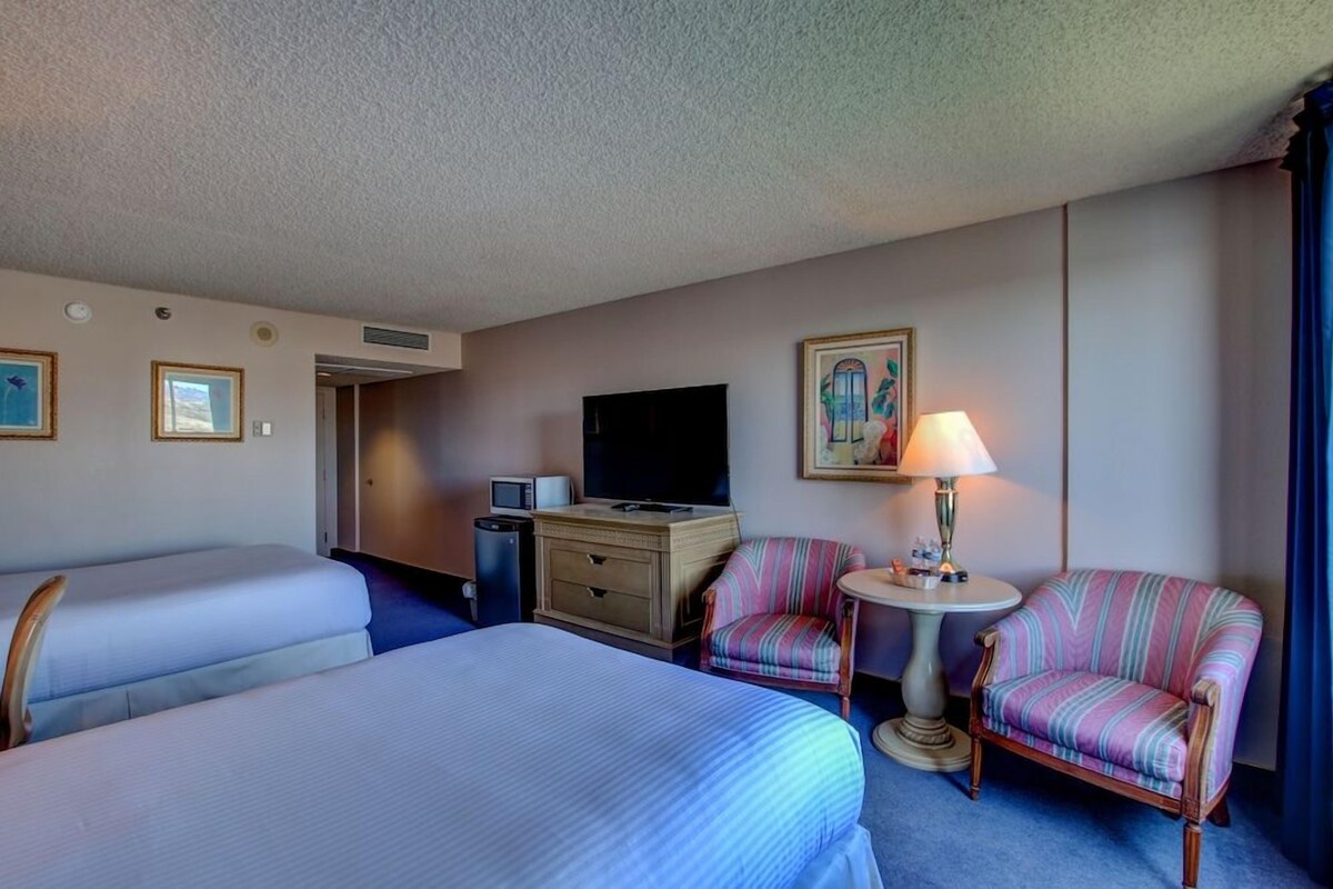 A hotel room with two beds, a TV, a desk with a lamp, and a chair.