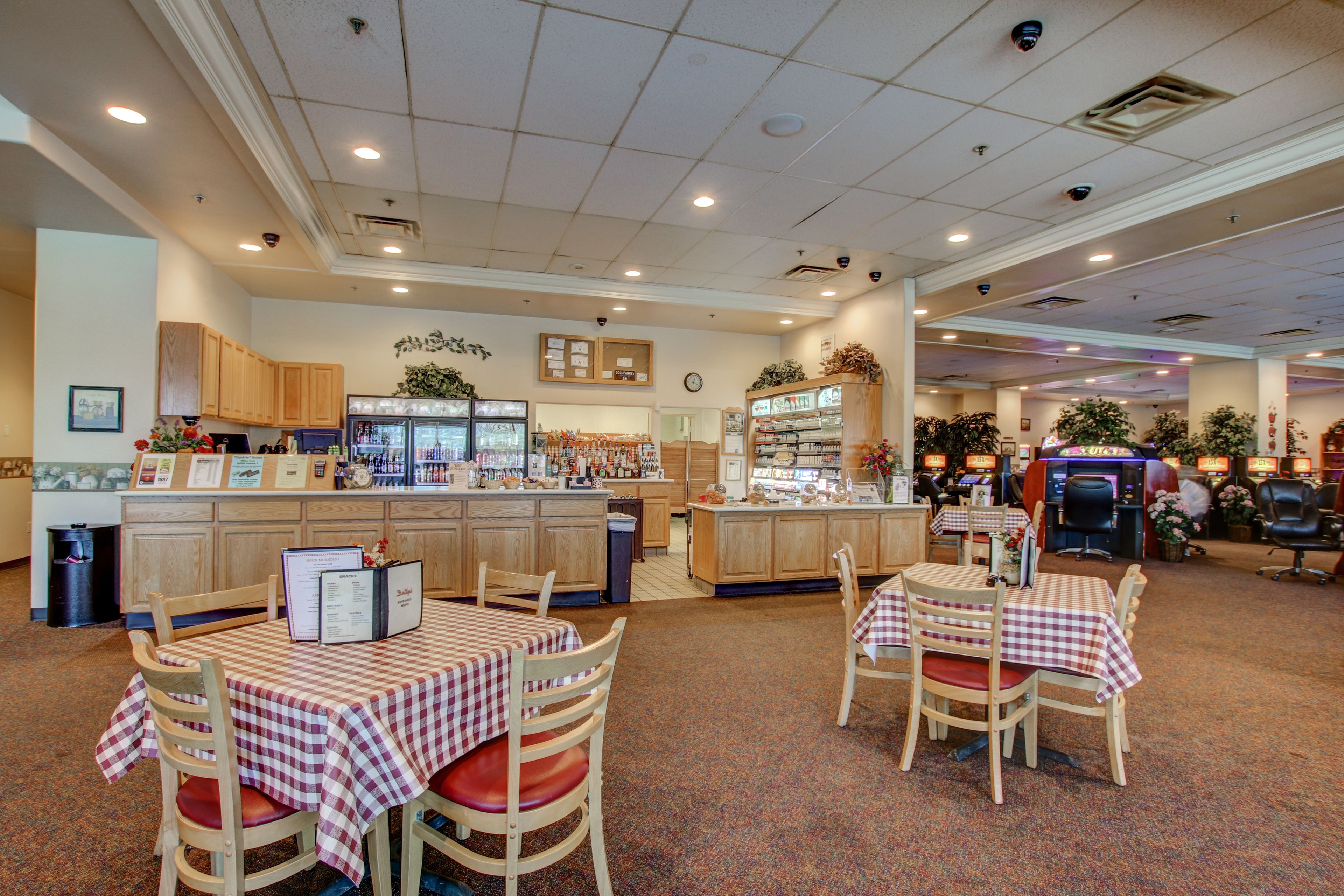 A restaurant with checkered tablecloths, wooden chairs, a counter with a menu, and a clock on the wall.