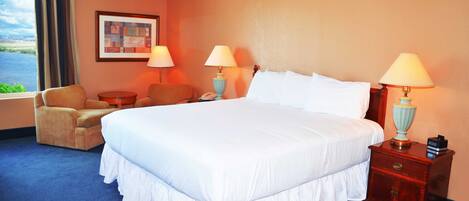A hotel room with a large bed, two bedside lamps, a chair, a small table, and a window with a view of the outdoors.