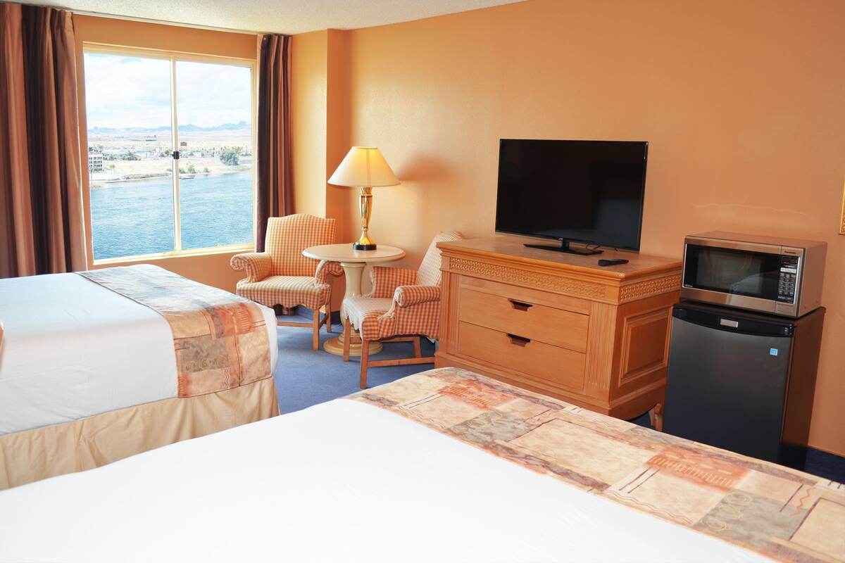 A hotel room with two beds, a television, a microwave, and a view of a body of water.