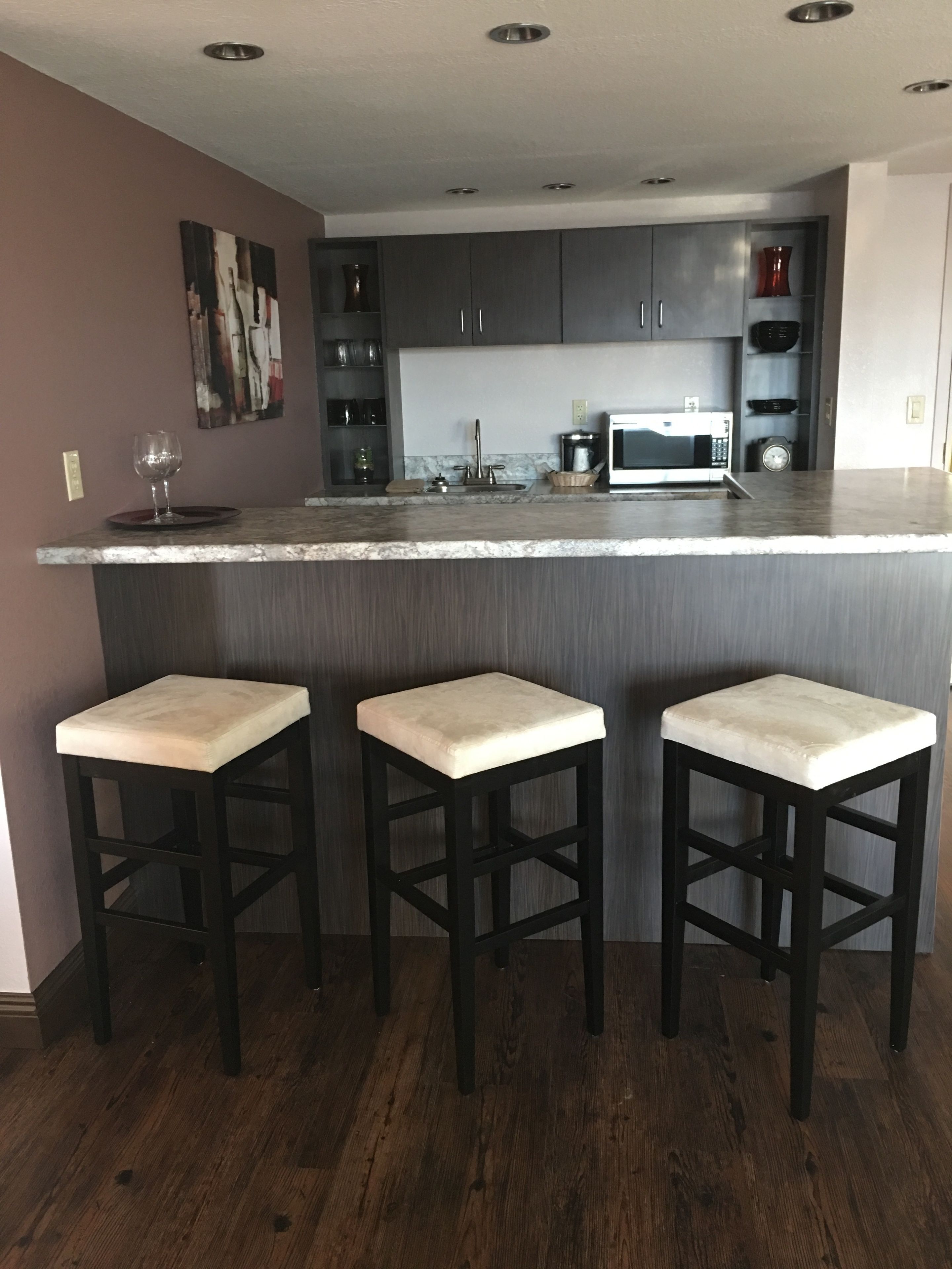 Een moderne keuken met een centraal eiland, donkerhouten barstoelen en een magnetron.