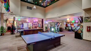 Un grand espace intérieur comprenant une table de ping-pong, des jeux d’arcade et un coin salon avec des chaises et des tables.