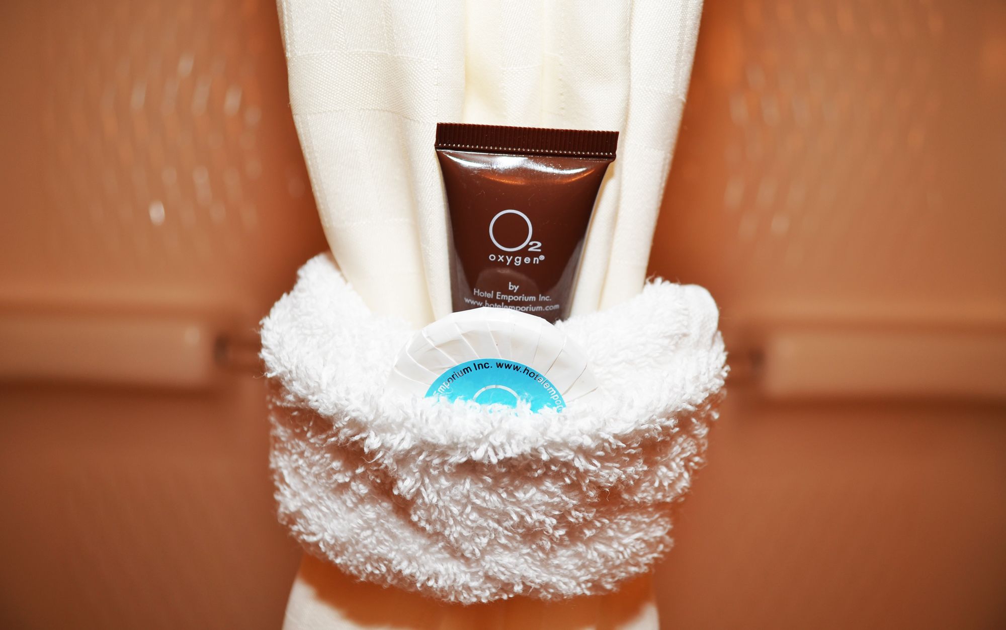 Un baño con un perchero que sostiene una toalla blanca y un tubo marrón de O2, cortesía de Hotel Emporium Inc.