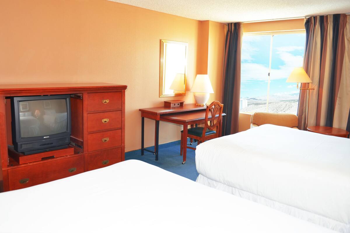 A hotel room with a bed, a desk with a lamp, a television, and a view of the beach.