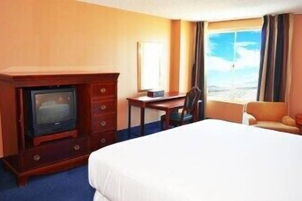 A hotel room with a bed, a TV, a desk, and a window with a view.