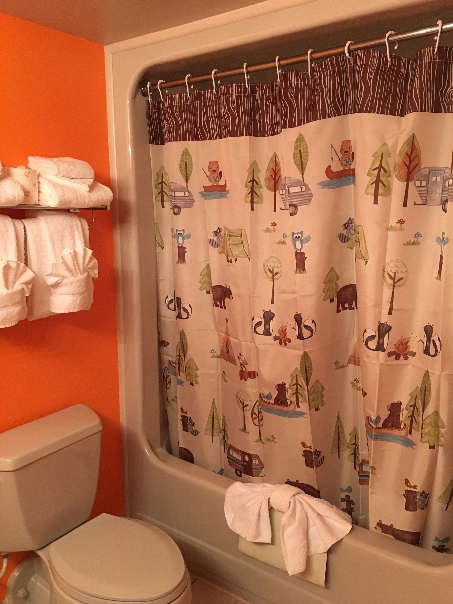 A bathroom with an orange wall, a white toilet, and a shower curtain with animal and nature patterns.