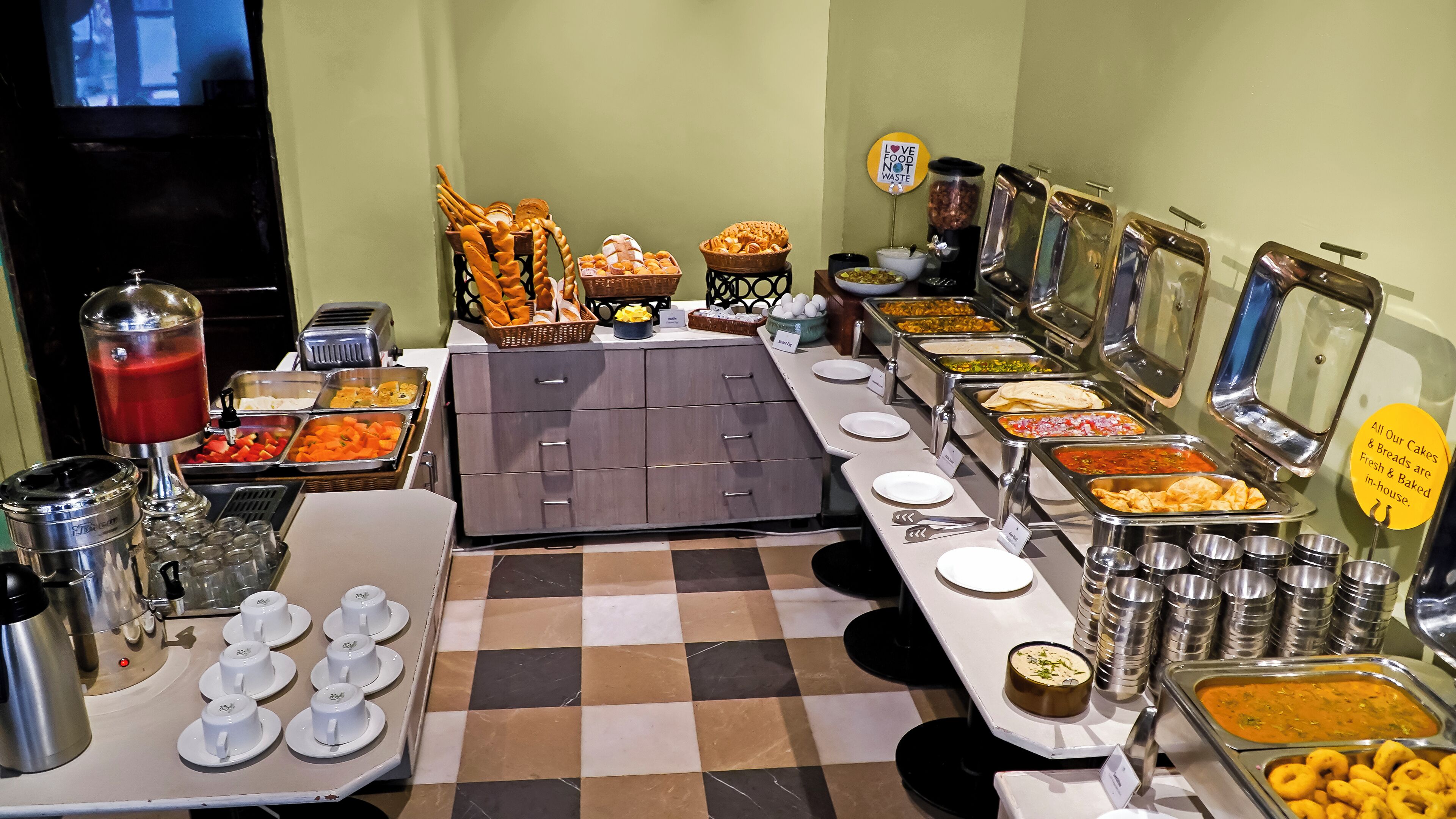 A buffet setup with various food stations, including a fruit bowl, bread, and a beverage dispenser.
