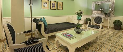 A living room with a sofa, chairs, a coffee table, a floor lamp, and framed pictures on the wall.