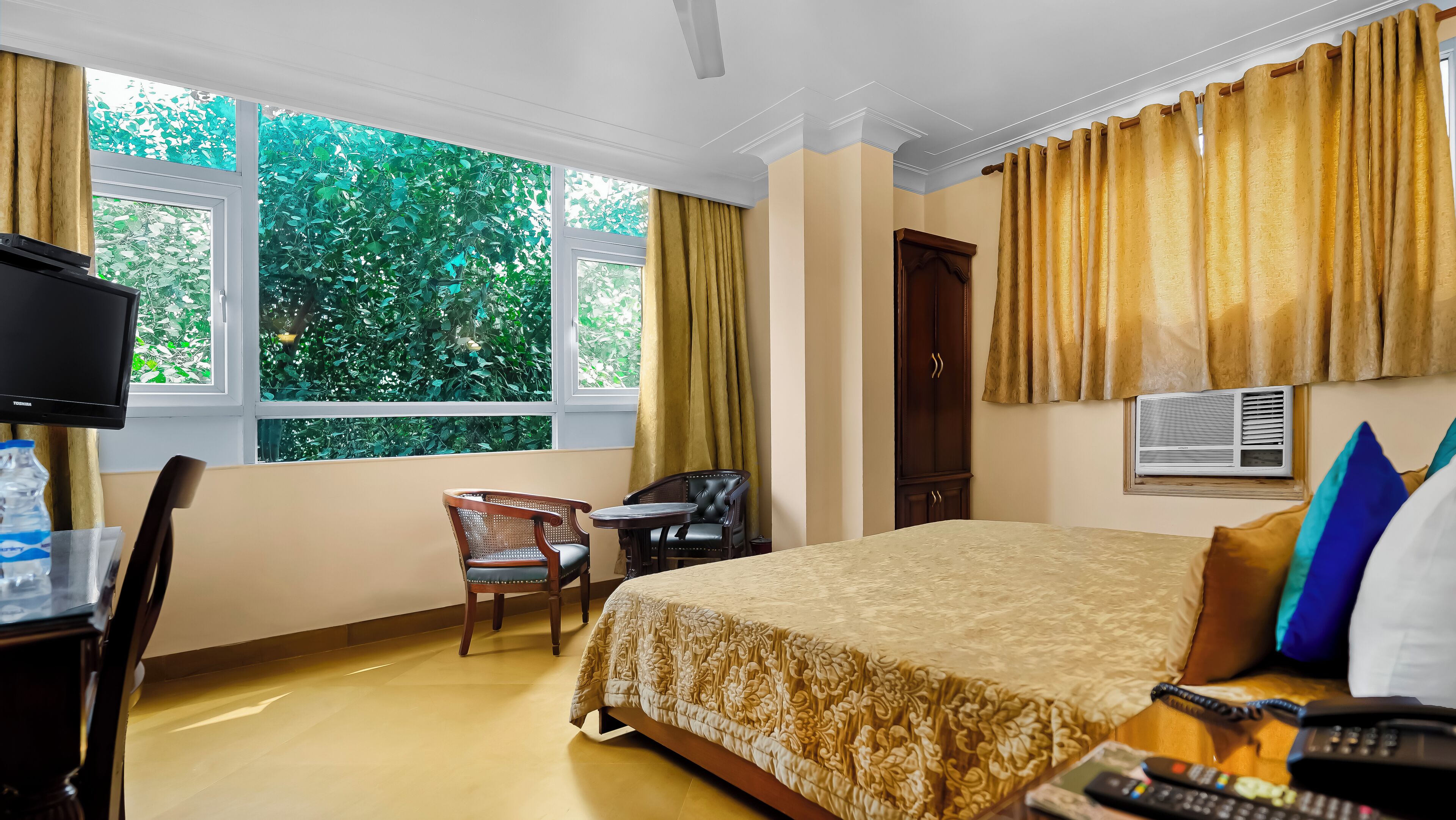 A hotel room with a bed, a desk with a TV, a chair, and a window with curtains.