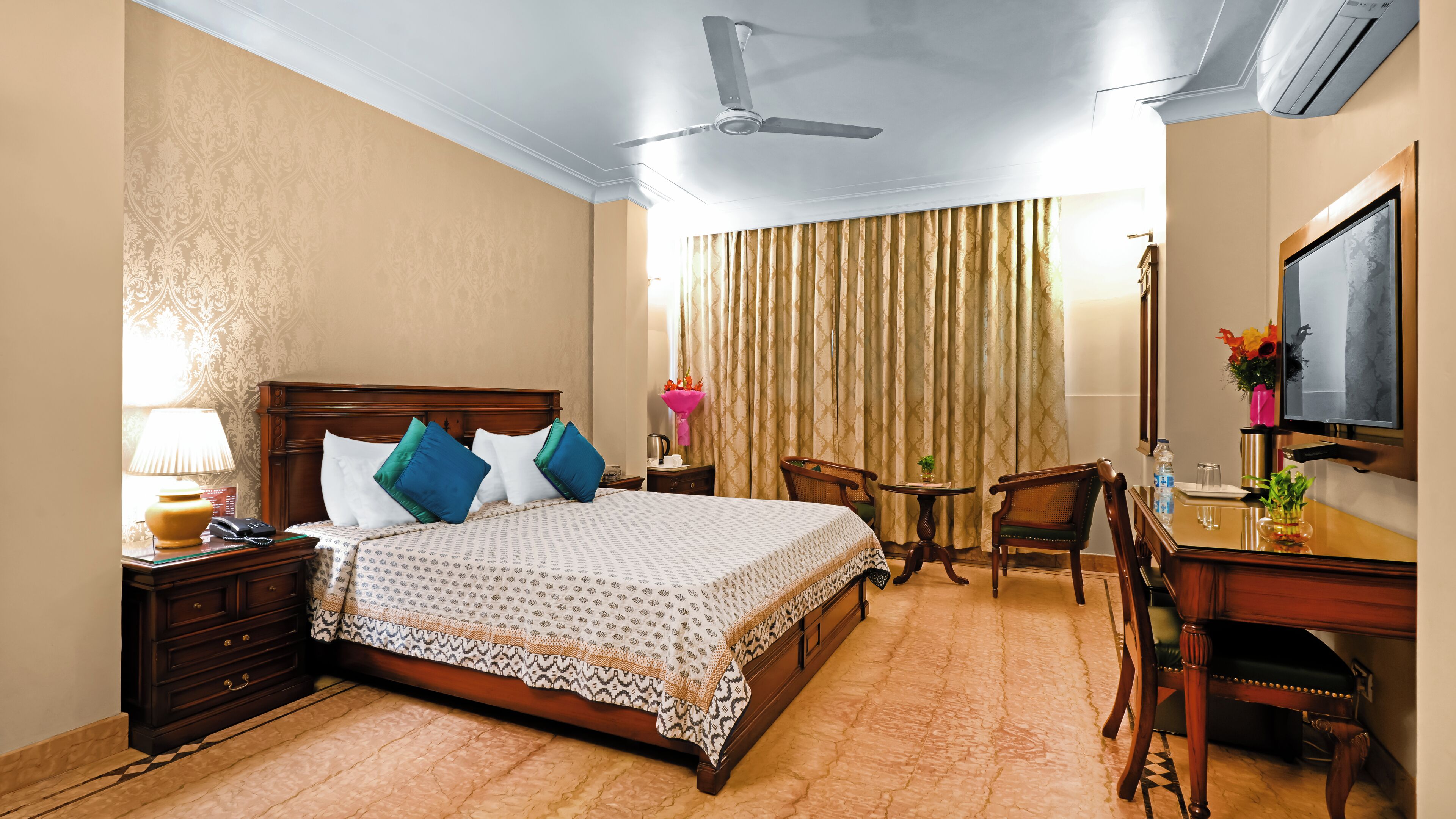 A hotel room with a bed, a desk, a chair, a television, and a ceiling fan.
