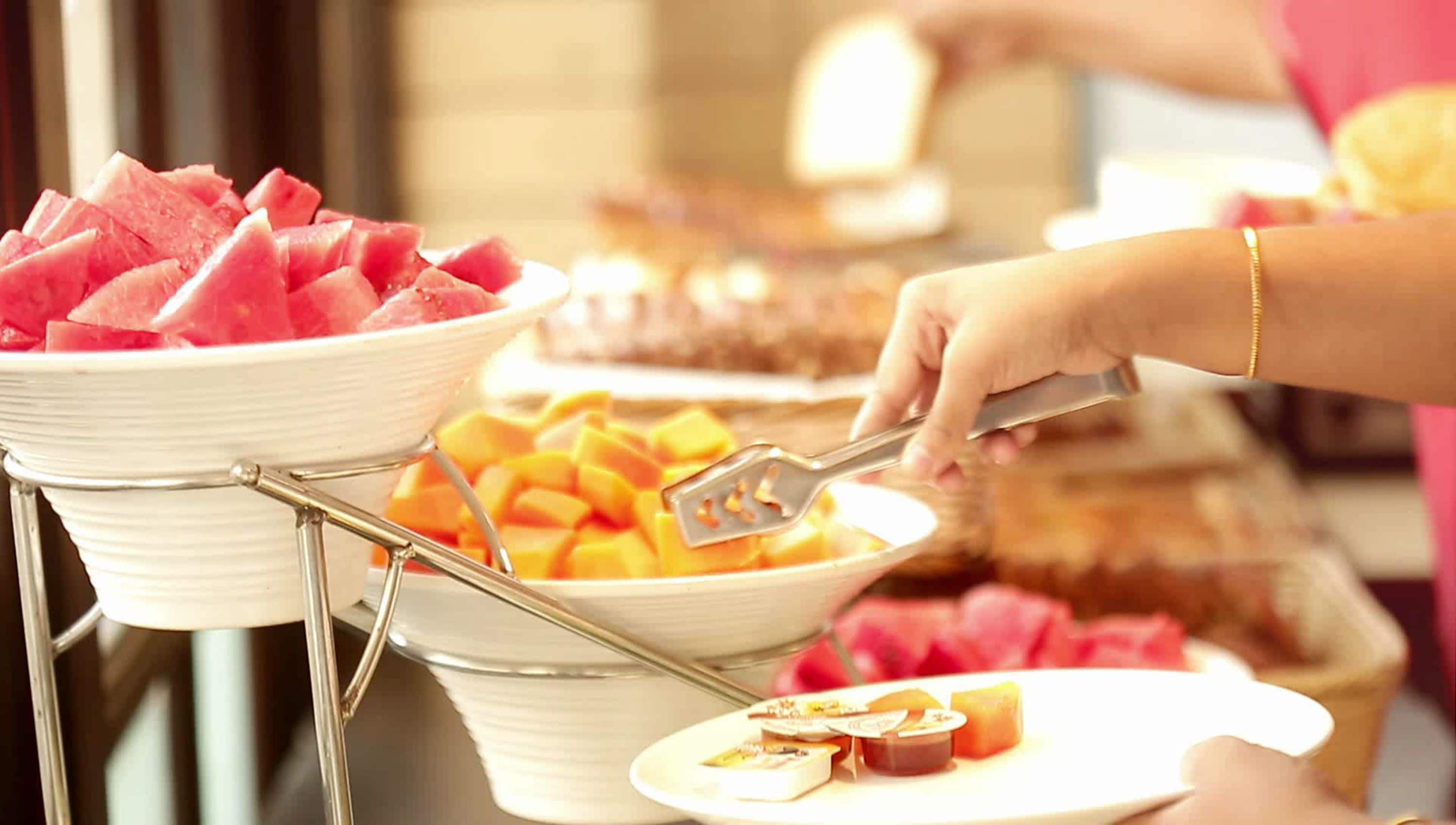 A buffet setup with various food items including watermelon and mango.