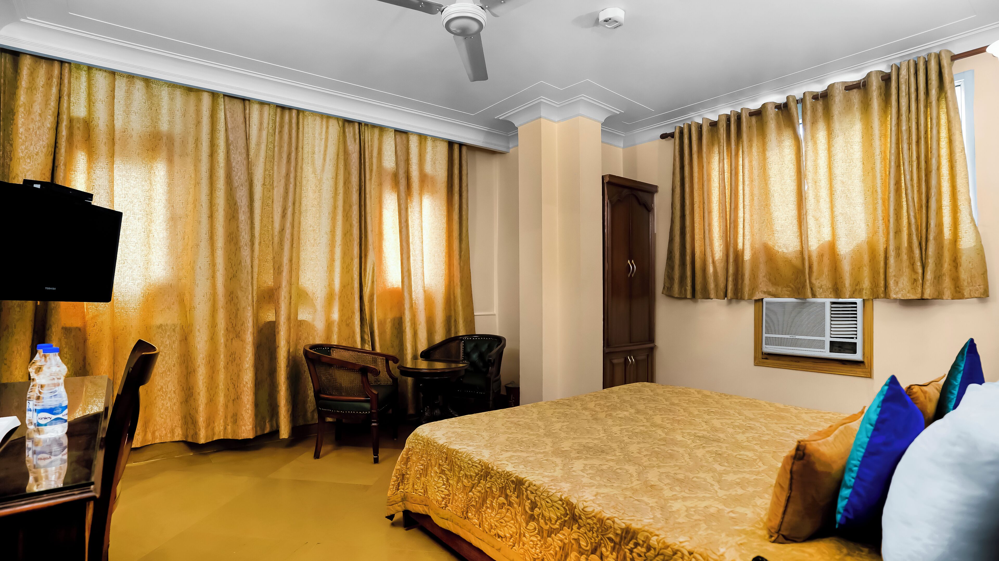 A hotel room with a bed, a desk with a television, a chair, and a wardrobe.