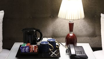 A hotel room with a bedside table featuring a coffee maker, two cups, a telephone, and a tray with snacks.