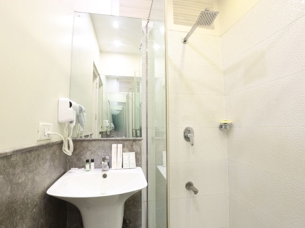 Une salle de bain équipée d’un lavabo, d’un sèche-cheveux, d’un miroir et d’une douche.