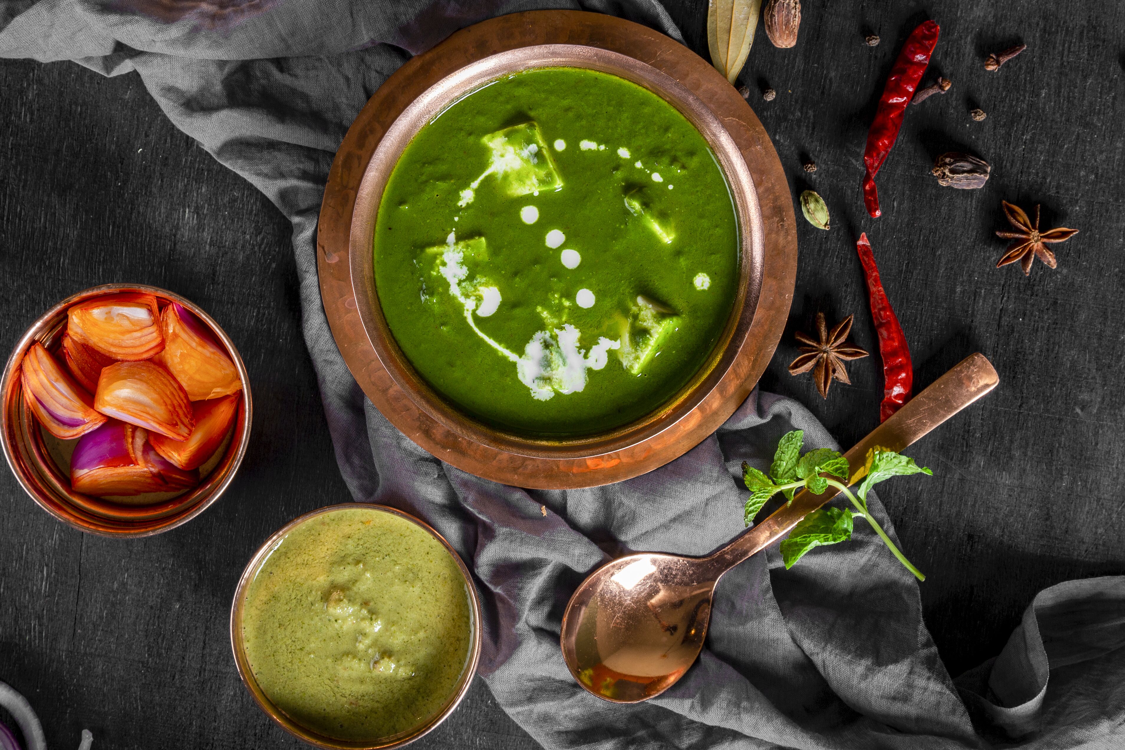 A bowl of green soup with cubes, a spoon, and a cloth.