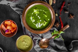 Una ciotola di zuppa verde con dadini, un cucchiaio e uno strofinaccio.