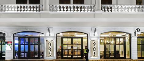 L’entrée d’un hôtel avec un double portail, une personne en uniforme et un balcon situé à l’étage supérieur.