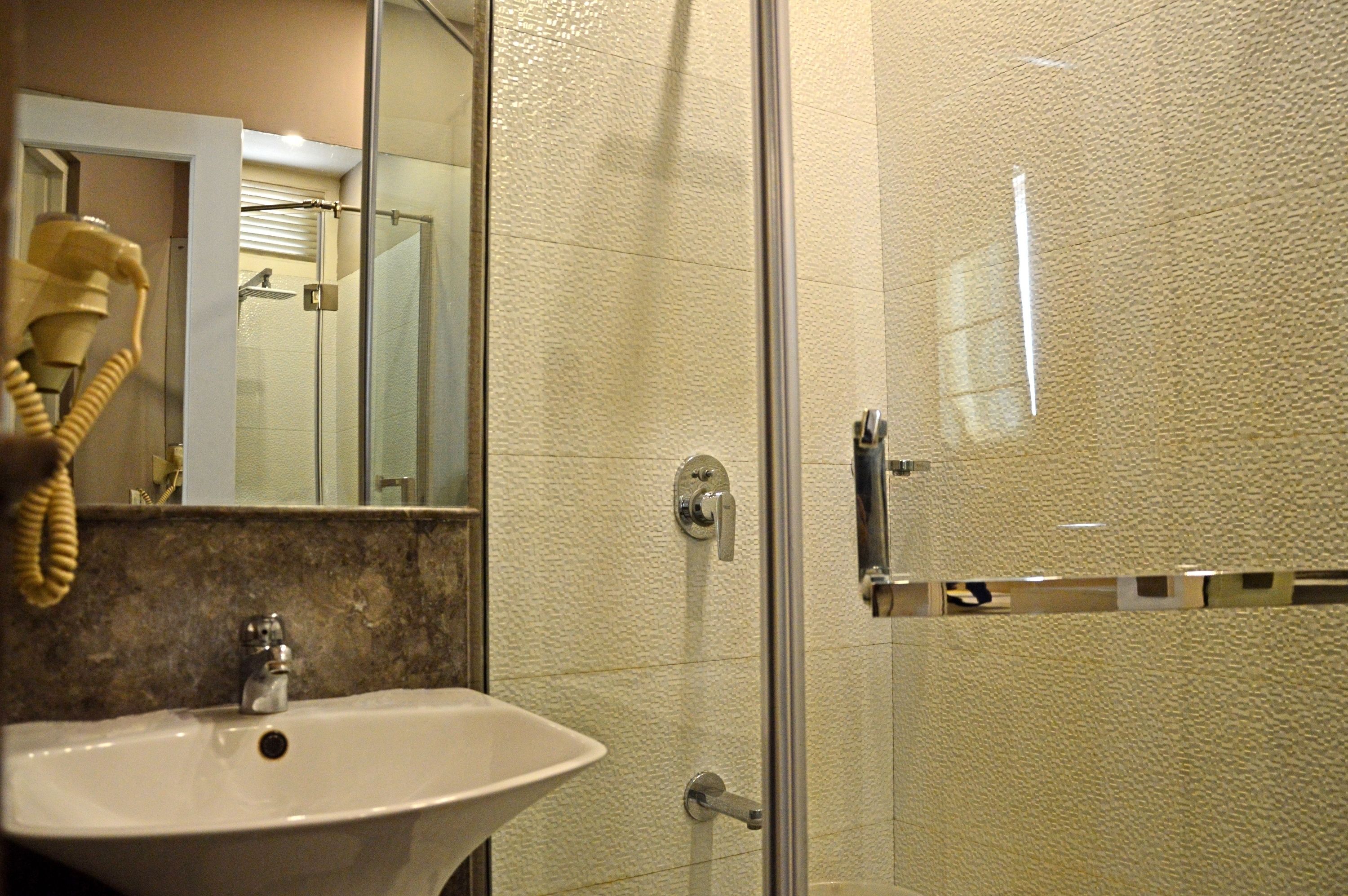 Baño con lavamanos, espejo y cabina de ducha de vidrio.