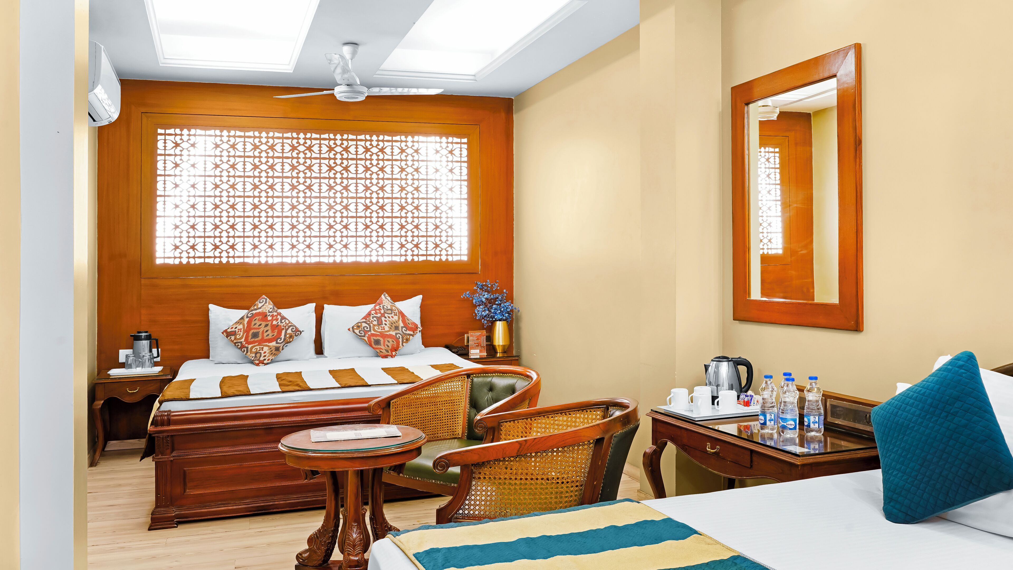 A hotel room with a bed, a desk with a chair, a small table, and a window with a decorative screen.