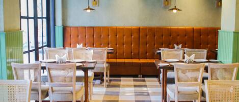 A restaurant with a checkered floor, wooden tables, wicker chairs, and a brown cushioned bench.