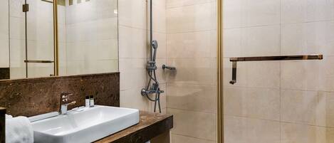 Une salle de bain moderne avec un grand lavabo, une douche équipée d’un pommeau de douche à main et un miroir avec un cadre doré.