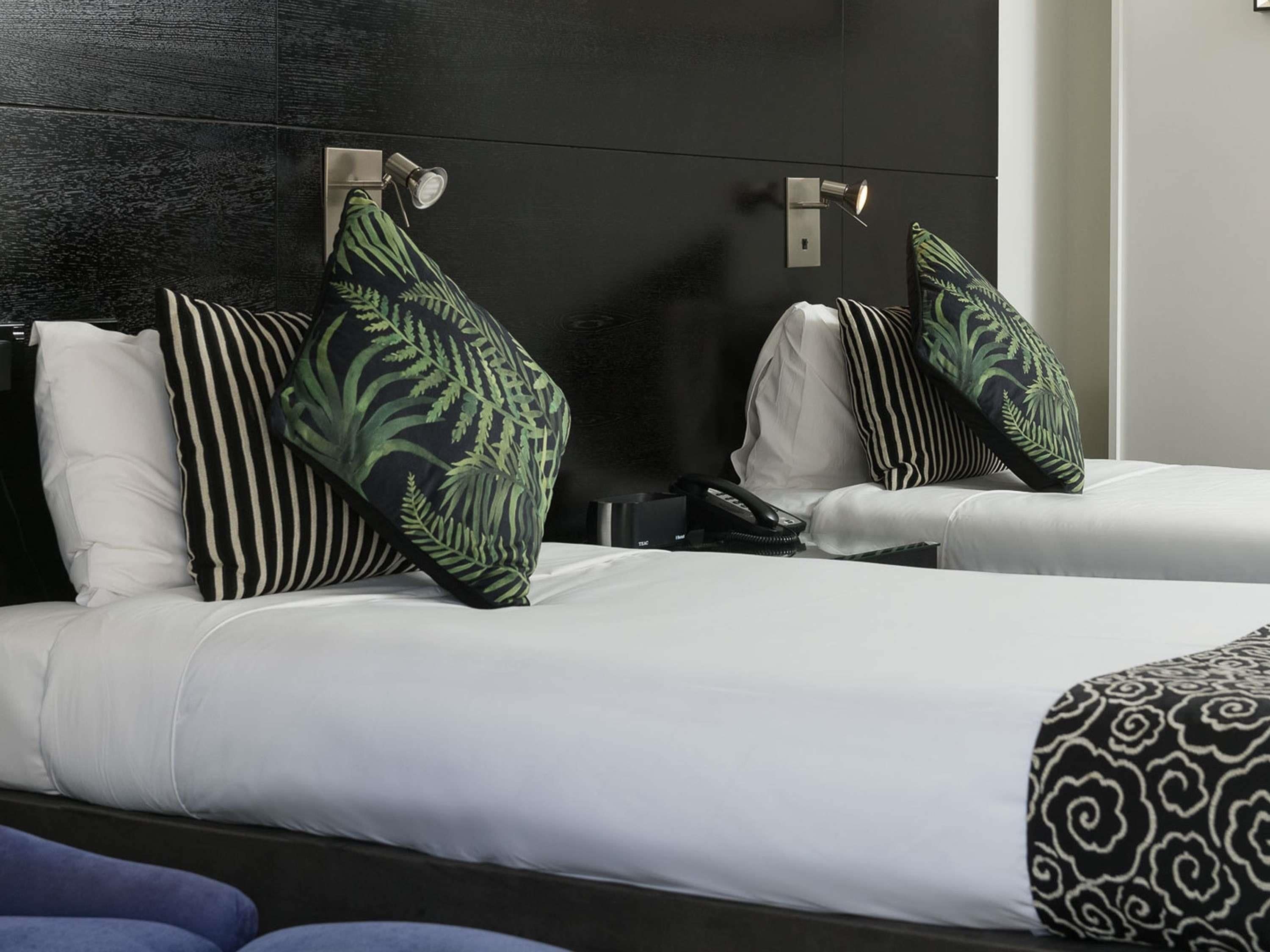 Une chambre d’hôtel avec deux lits, chacun étant équipé d’un oreiller et d’une table de chevet.