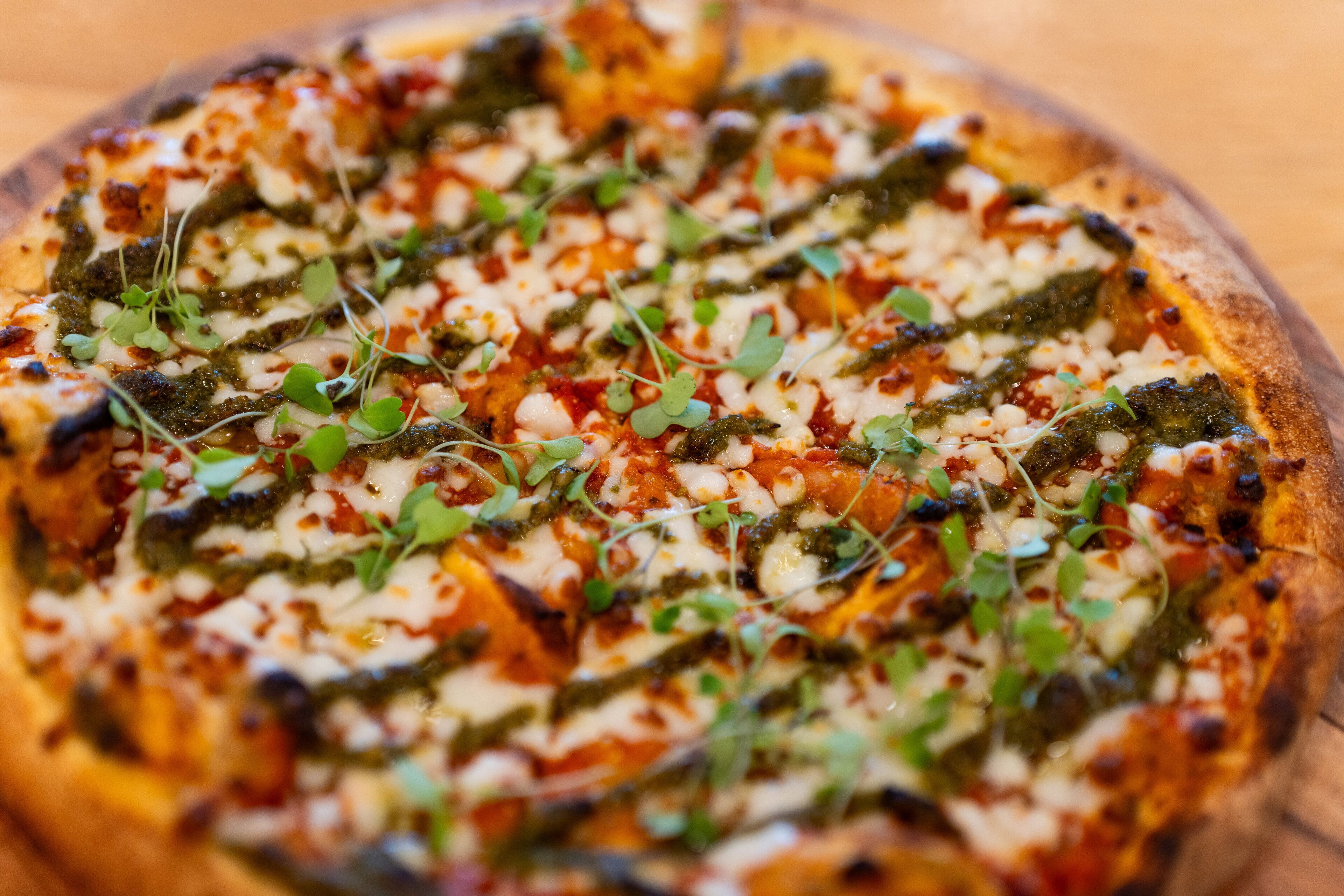 A pizza with green pesto and cheese on a wooden table.