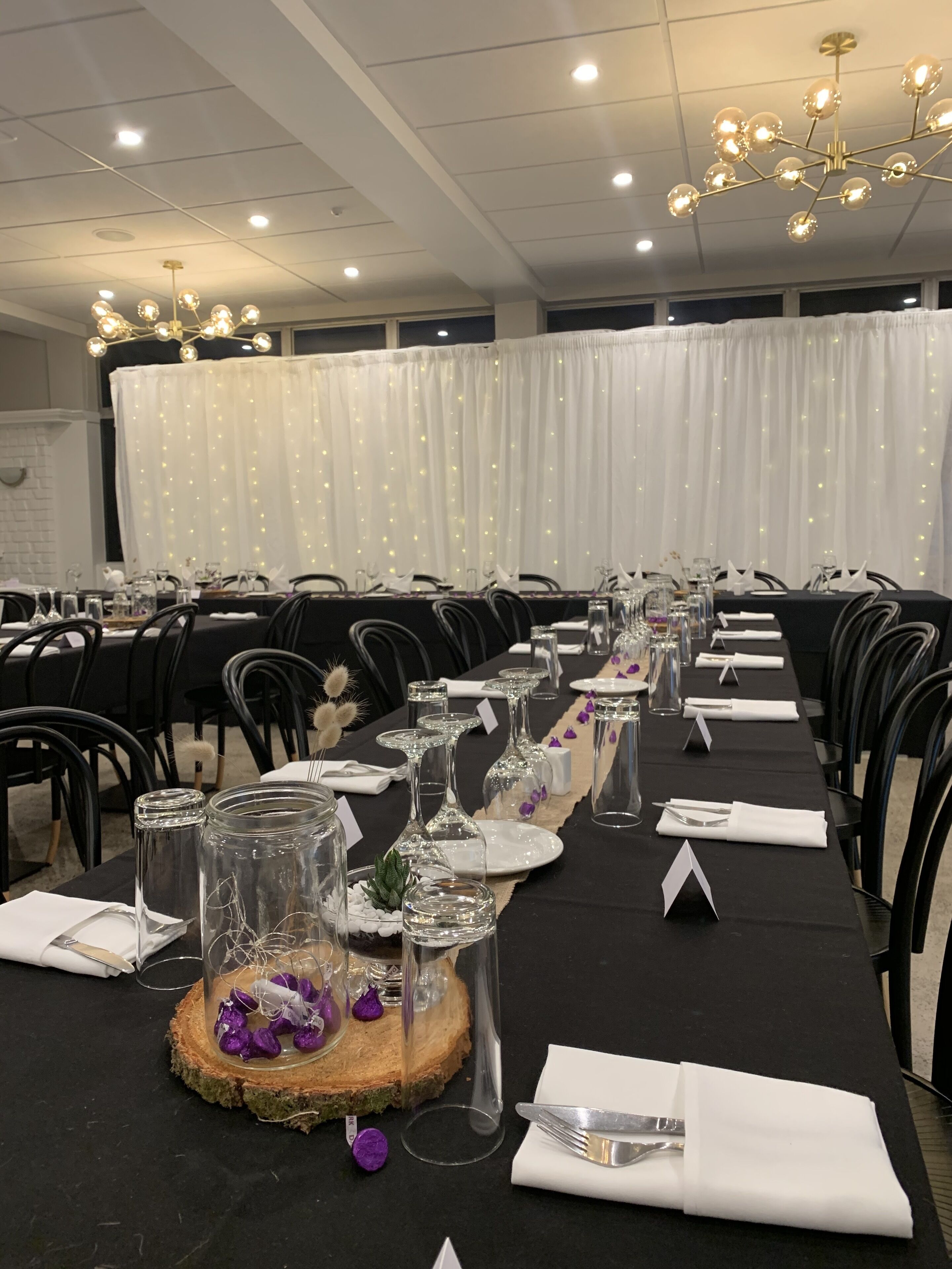 A banquet hall with long tables set for a formal event, featuring glassware, napkins, and centerpieces.