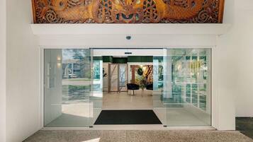 A modern building entrance with glass doors, a reception desk, and a decorative wall above.